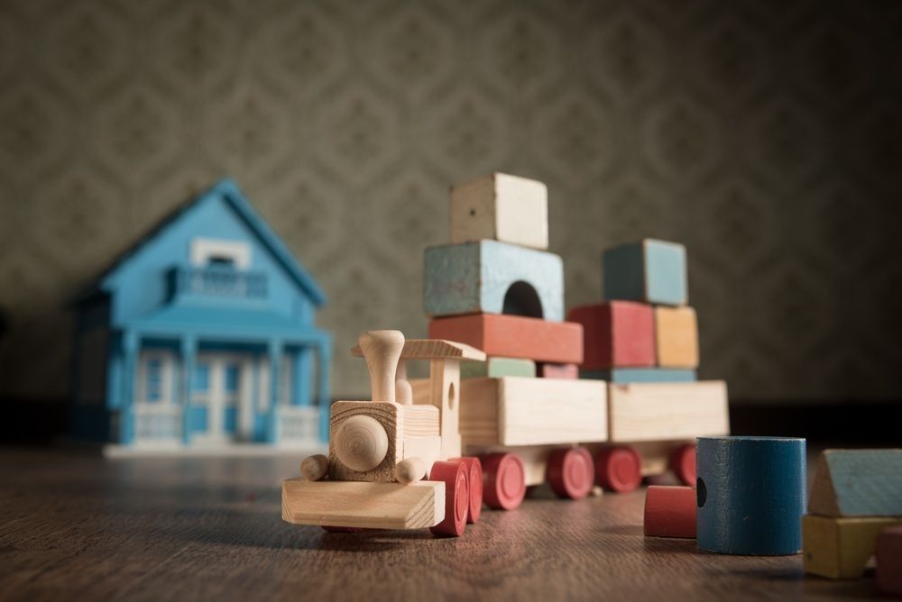 Wooden train and doll house on the floor with vintage wallpaper on background.