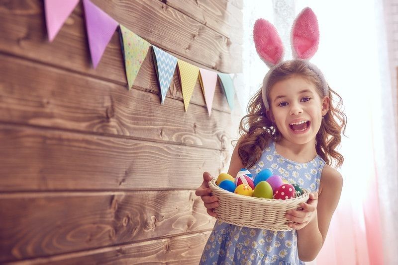 Cute little child wearing bunny ears holding basket with painted eggs on Easter day. 