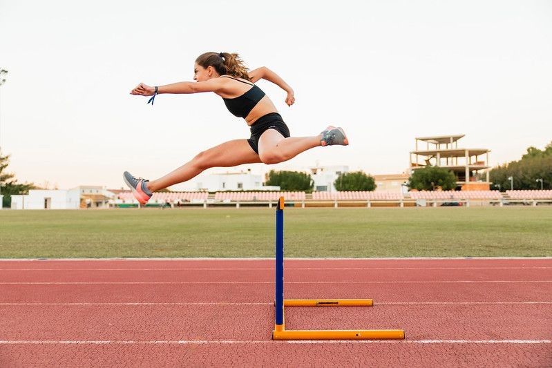 Female Athlete jumping over the hurdle while running on track.