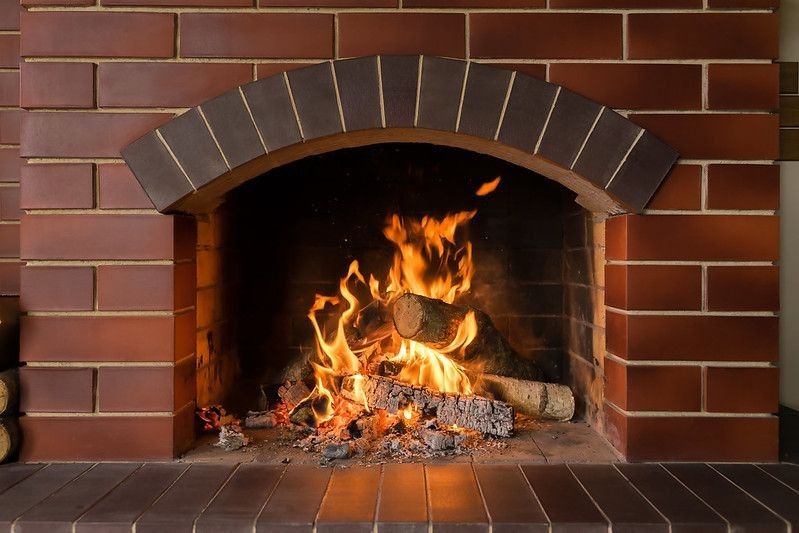 A brick fireplace in which a fire burns.
