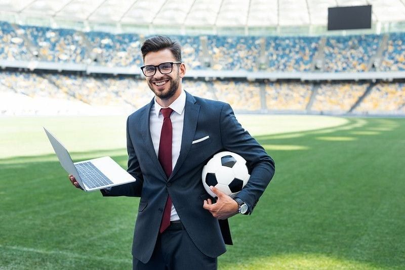 Man holding football and laptop in stadium