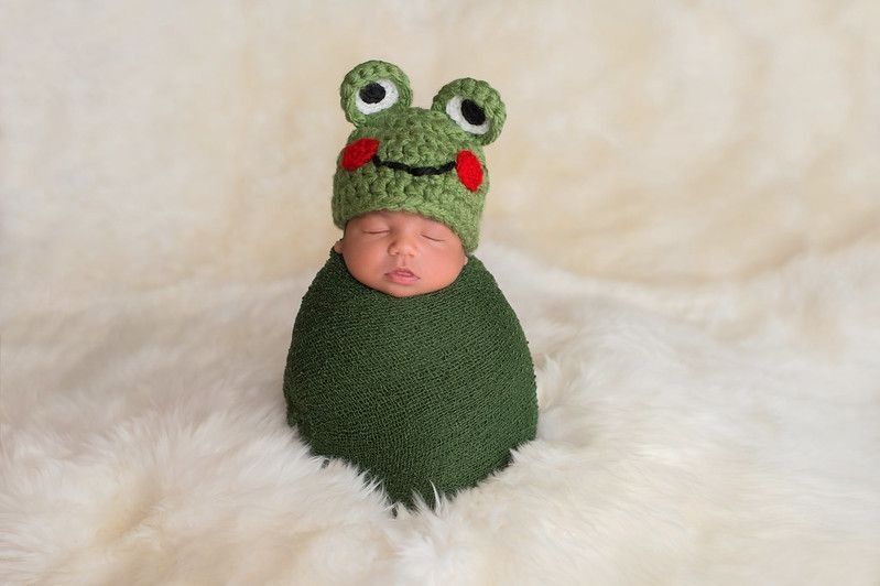 Nine day old newborn baby boy wearing a green frog hat.