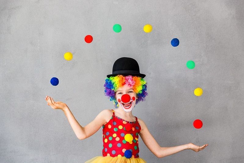 A kid dressed as a Circus Clown is juggling colorful balls in hands.