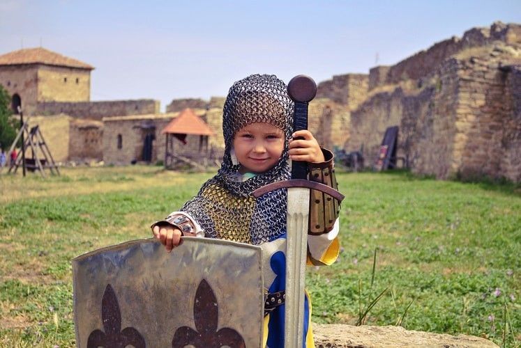 a small but very brave girl in armour and chain mail with sword and shield in a medieval castle