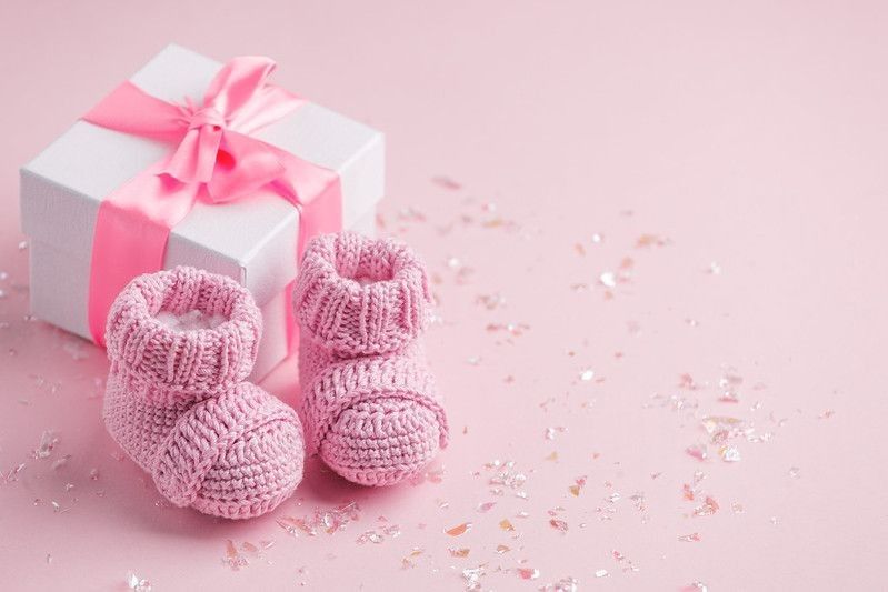 Pair of small baby socks and gift box on pink background