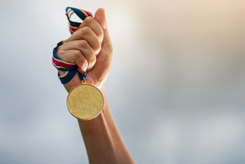 Hand holding gold medal on sky background.