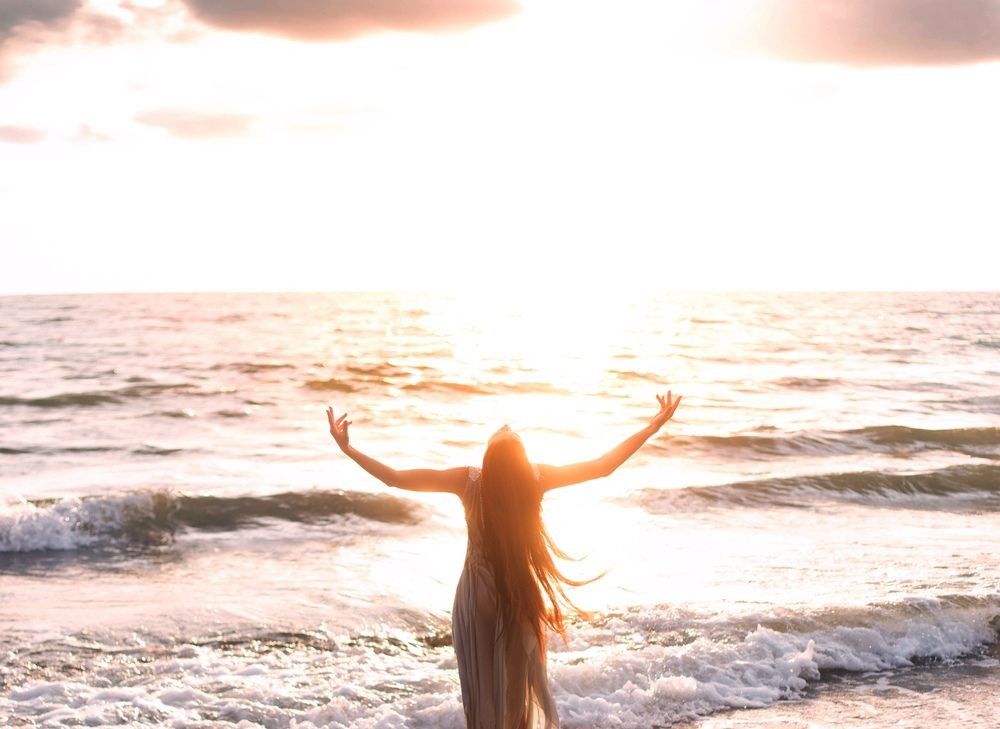 happy woman stands seashore turned away hand raised to heaven sky sun light.