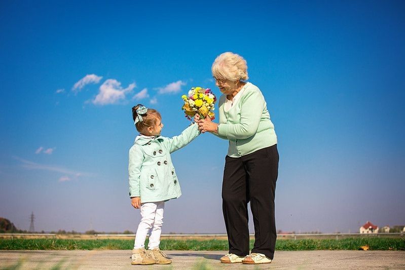 happy granddaughter giving flowers to grandmother outdoors representing national be nice day.