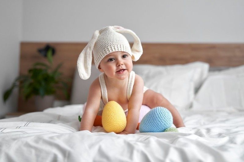 Little baby in rabbit costume sitting on bed at home