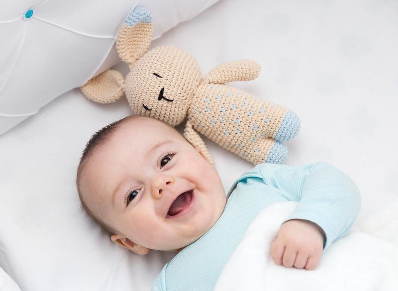 Happy baby newly awake in his crib and with his bunny doll.