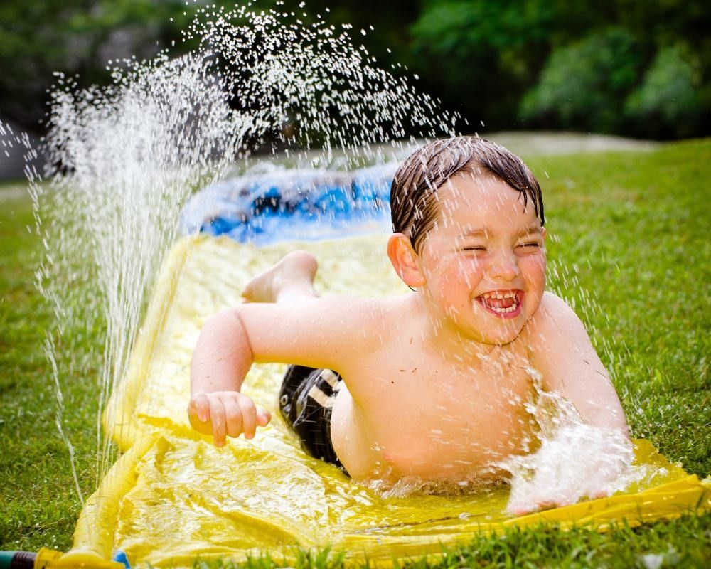 Happy child on water slide to cool off on hot day during spring.