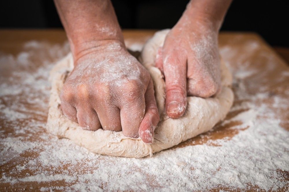 The cook kneads the dough with his hands on a wooden Board.