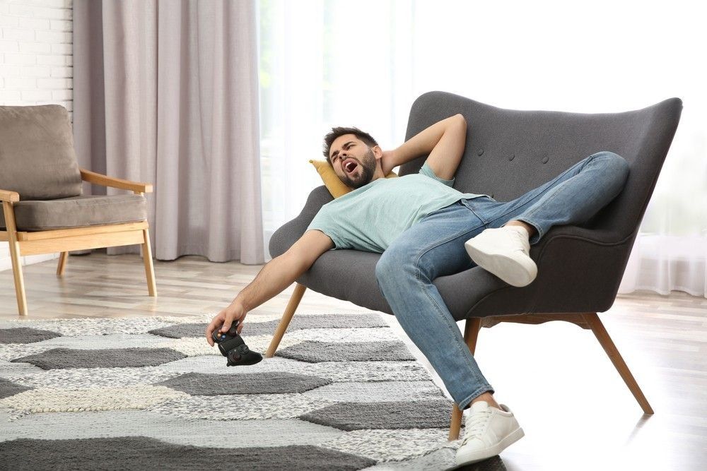 Lazy young man playing video game while lying on sofa at home.