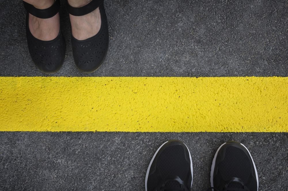 Legs of a couple standing opposite each other divided by the yellow asphalt line