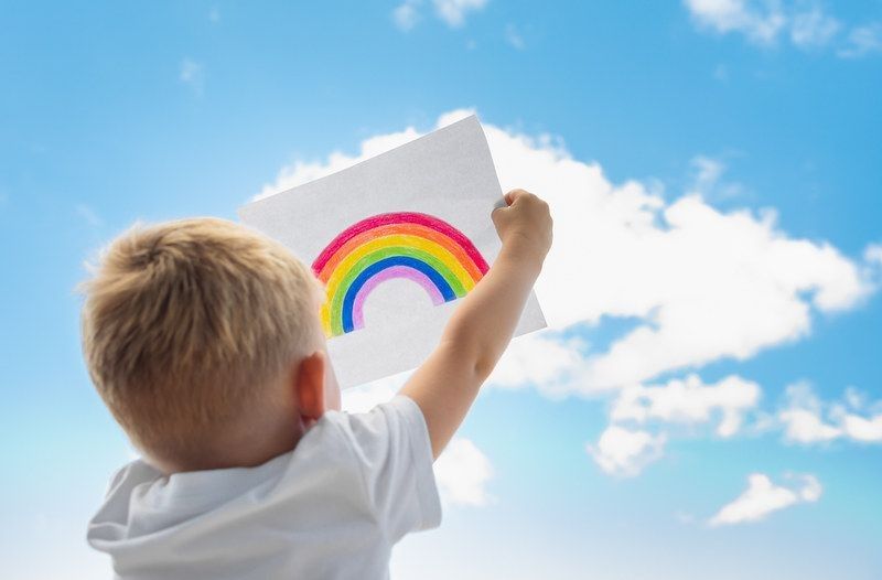 Little child holding up rainbow in the sky. 