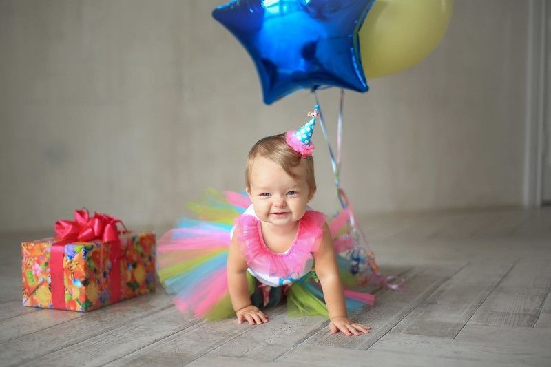 Little Baby girl wearing rainbow dress sitting with balloons and gift box