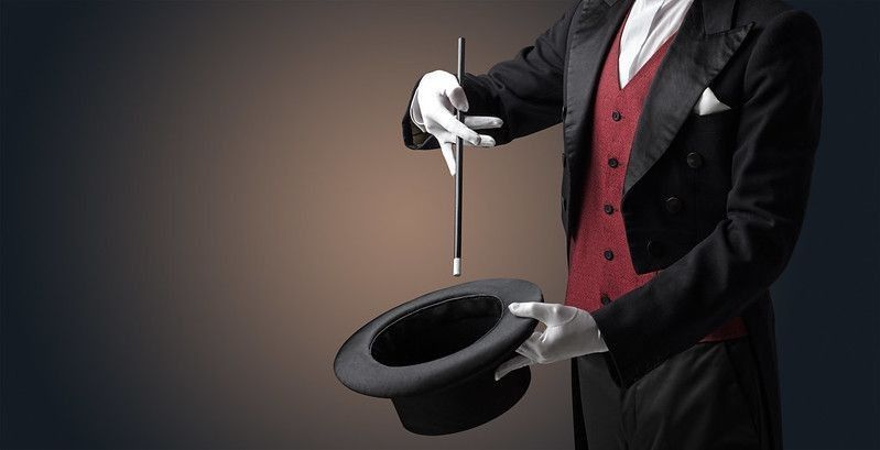 Illusionist white hand with a magic wand over a black hat.
