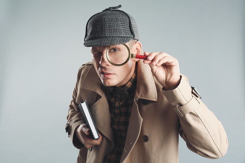 Male detective looking through magnifying glass.