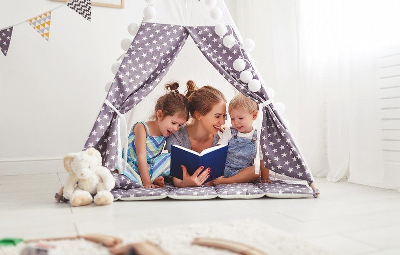 mother reading book to her children in a play tent