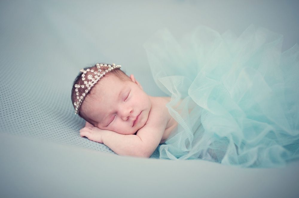Newborn baby girl with crown sleeping on green blue blanket.