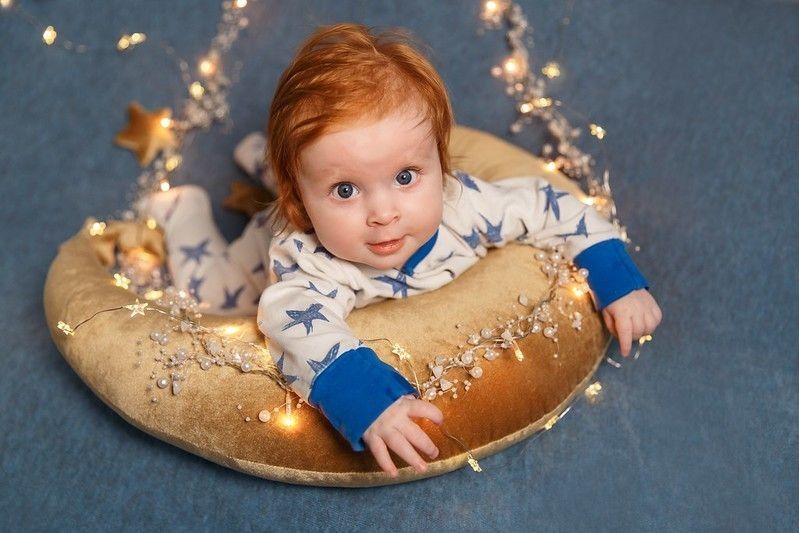 Infant baby lying on brown moon pillow with fairy lights and beads