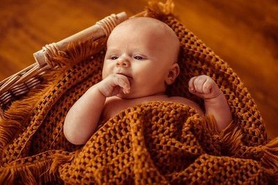 Newborn baby lying in a basket on brown knitted blanket