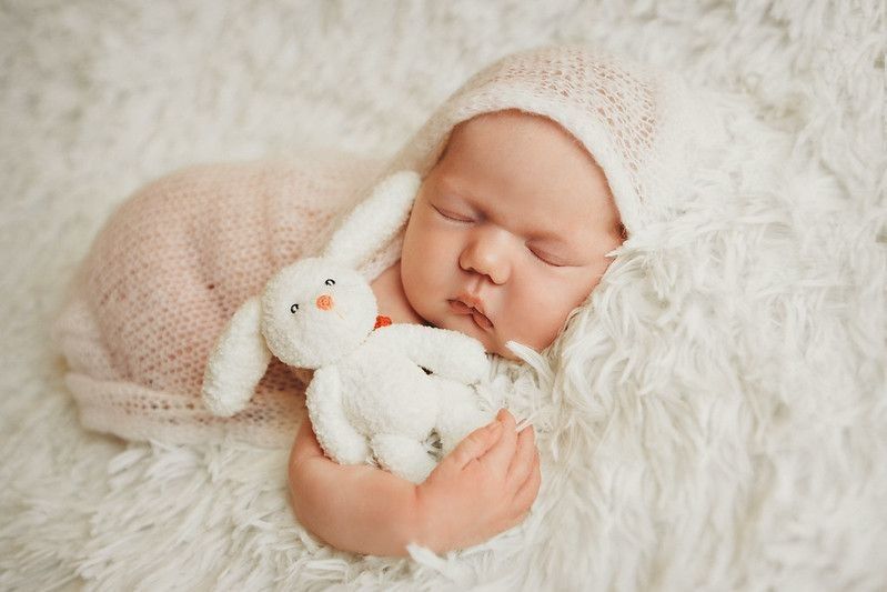 Newborn baby sleeping with white teddy bear.