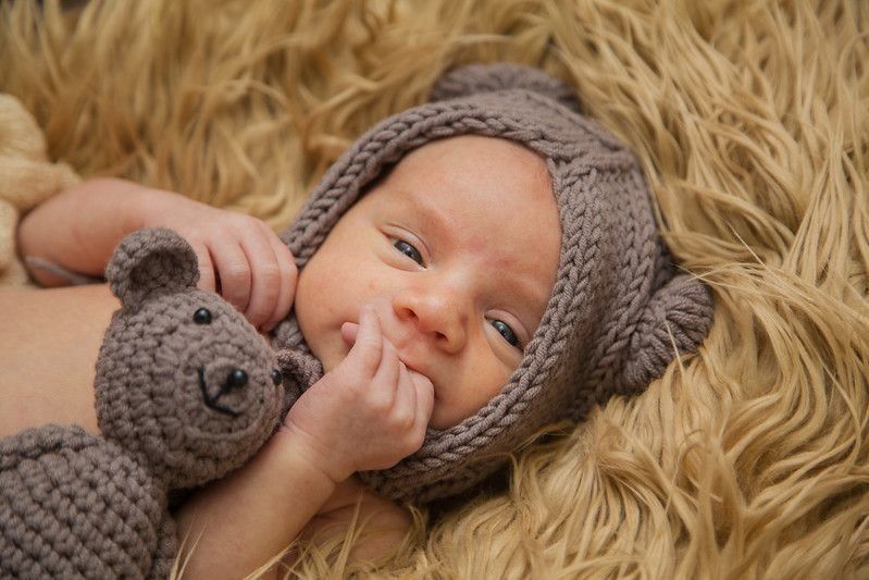 Newborn baby lying on brown fur with grey knitted teddy bear
