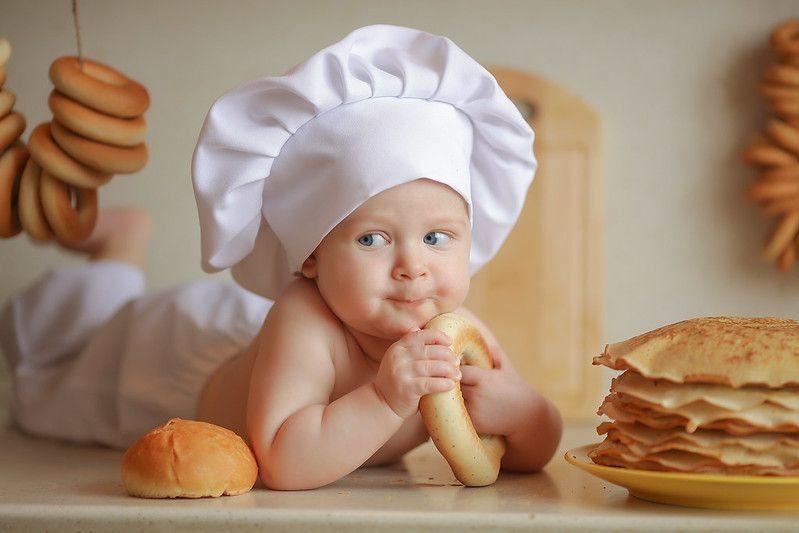 Cute newborn baby wearing chef hat and holdign pretzel