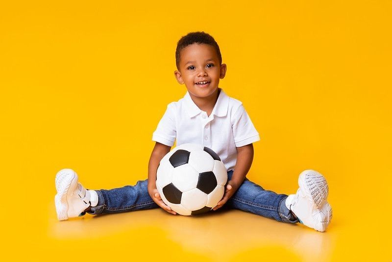 A little boy sitting with a football on yellow background