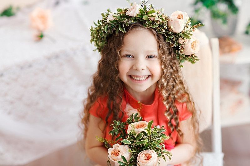 Young happy girl wearing floral crown is holding flower bouquet.