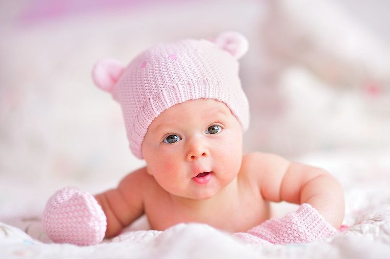 Baby Vanessa in pink knitted Bear hat and mittens on a bed - Nicknames