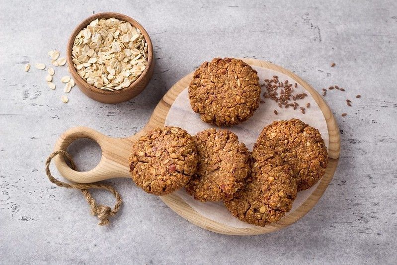 Healthy oatmeal cookies with dates, nuts and flaxseed on a wooden board on a gray textured background, top view.