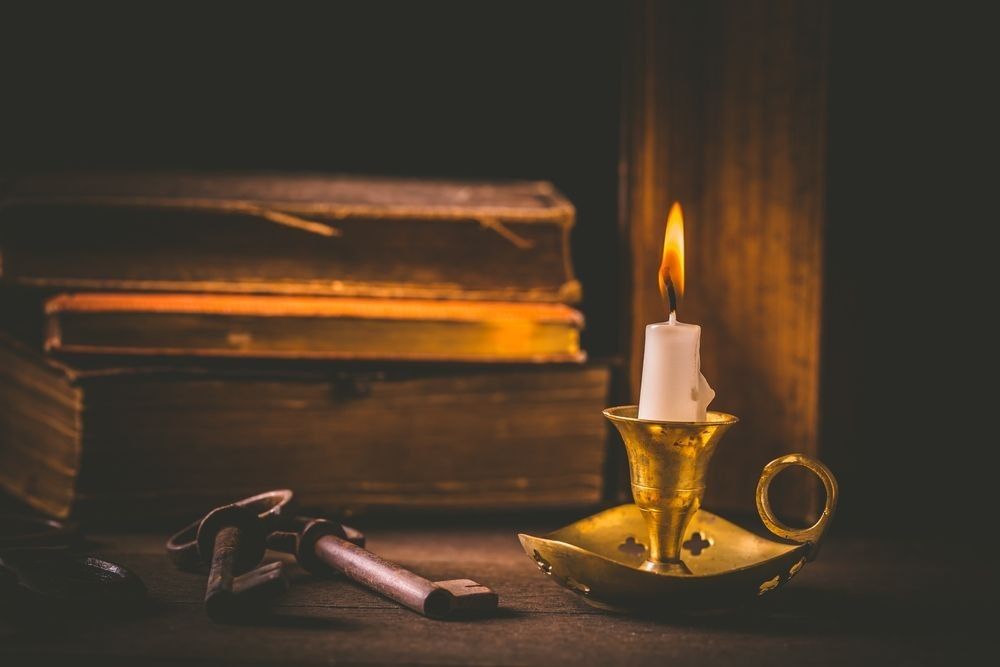 Pile of old antique books with candle and old rusty keys in vintage style on wooden black background.