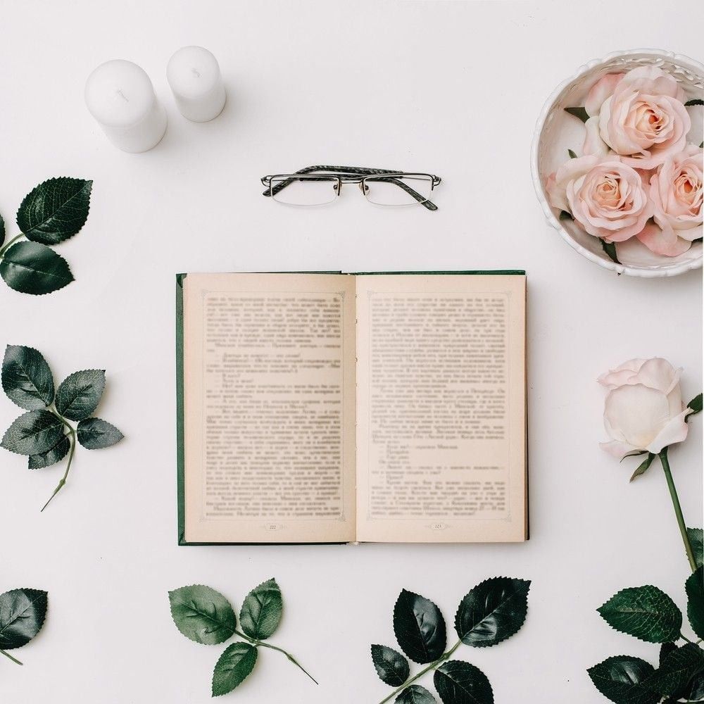Opened book, glasses, pink roses on white background.