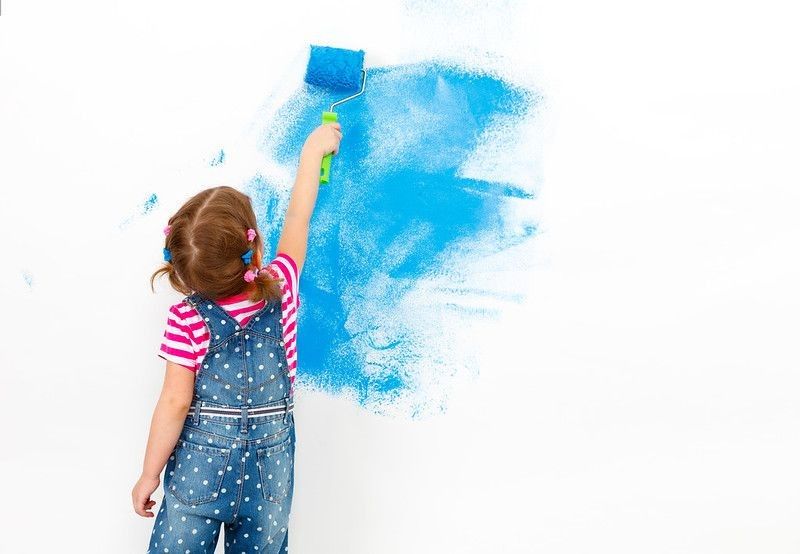  Happy child girl paints the wall with blue paint