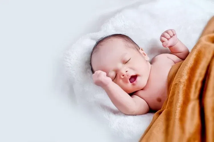 A newborn baby boy sleeping under a brown blanket