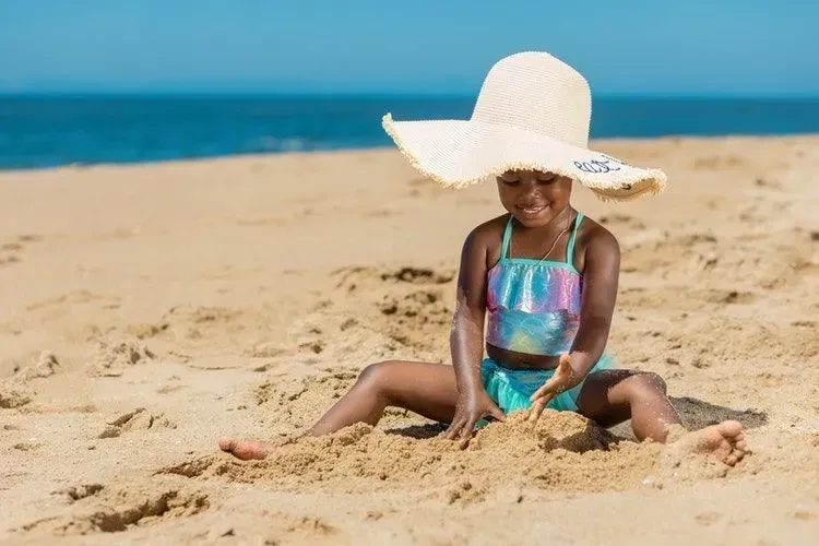 A little girl wearing mermaid dress is playing in sand on a beach