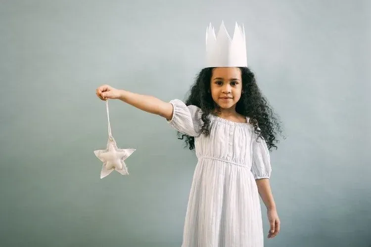 A little girl wearing a white crown is holding a star 