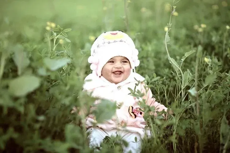 A happy baby girl sitting in green meadow