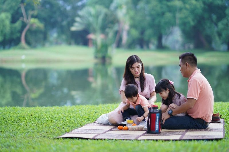 Cheerful Malaysian family having a  picnic near a lake in a public park on summer day.