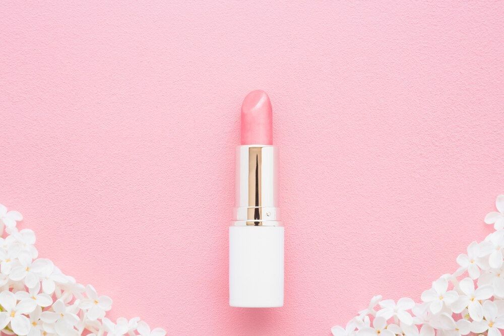 Pink lipstick with fresh lilac blossoms on light pastel background