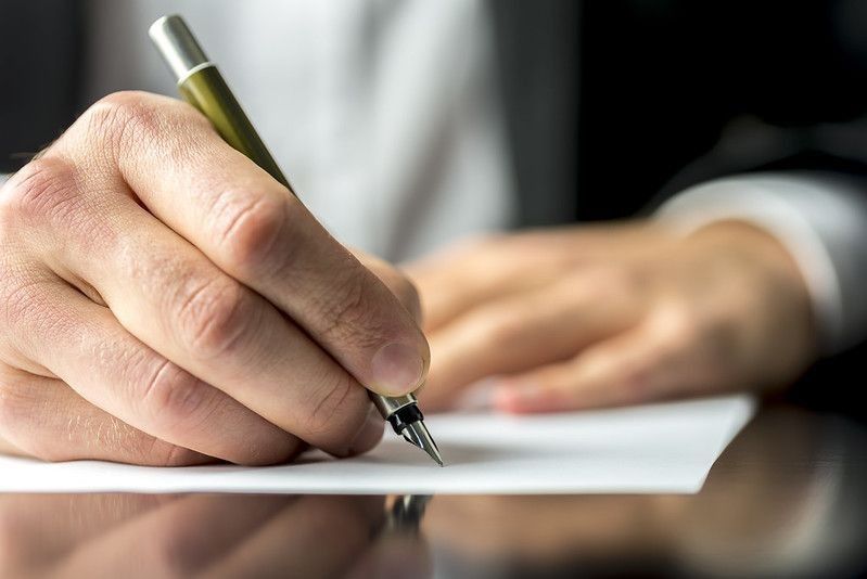 Close-up of the hands of a businessman in a suit signing or writing a document.