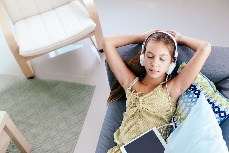 tween girl relaxing on a couch, listening to music in headphones and playing with tablet pc.
