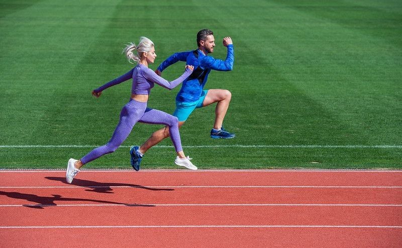 Athletic couple running on track at stadium.