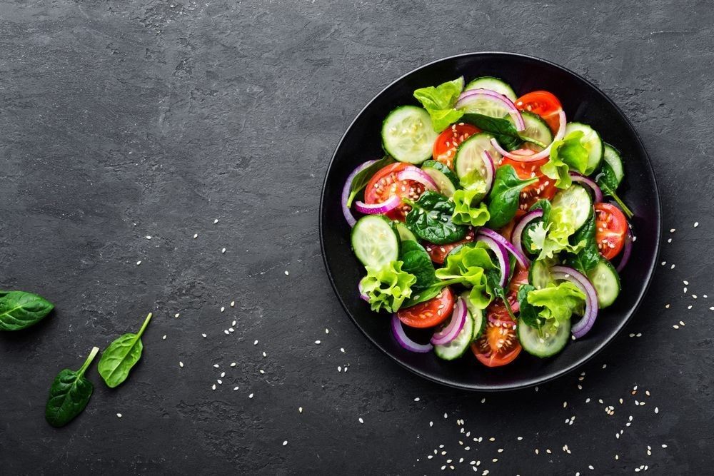 Healthy vegetable salad of fresh tomato, cucumber, onion, spinach, lettuce and sesame on plate.