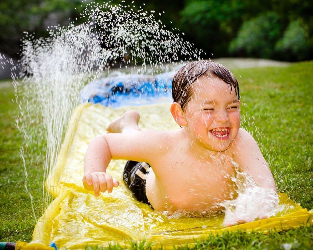 Happy child on water slide to cool off on hot day during spring or summer.