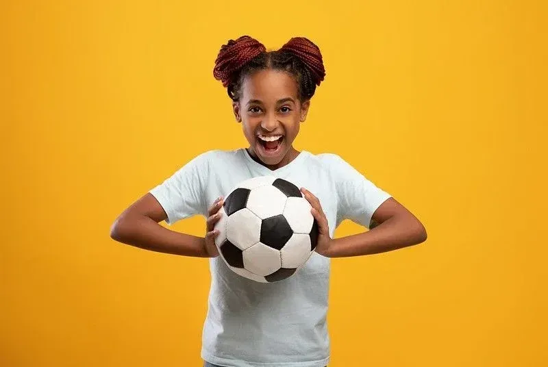 Happy teenage girl holding football on yellow background