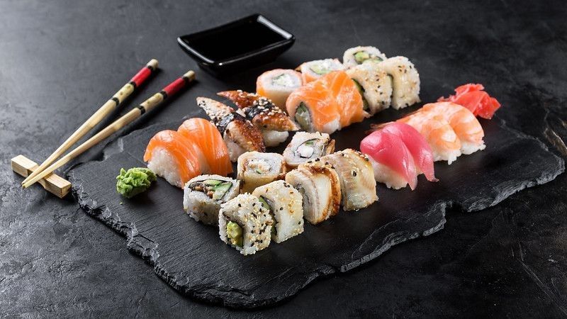 Sushi rolls set served on black stone slate on dark background.