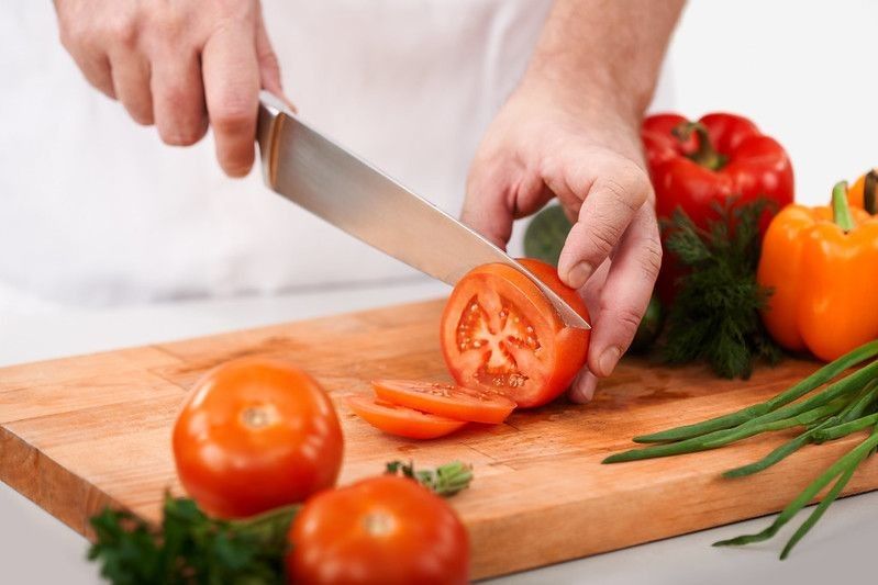 Chef cutting tomatoes with a sharp knife on wooden chopping board